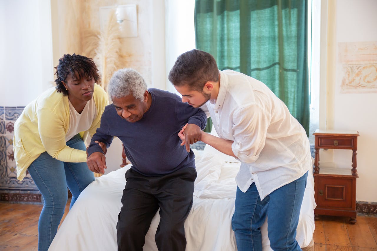 heros-img An elderly man receiving assistance from caregivers in a cozy home environment.